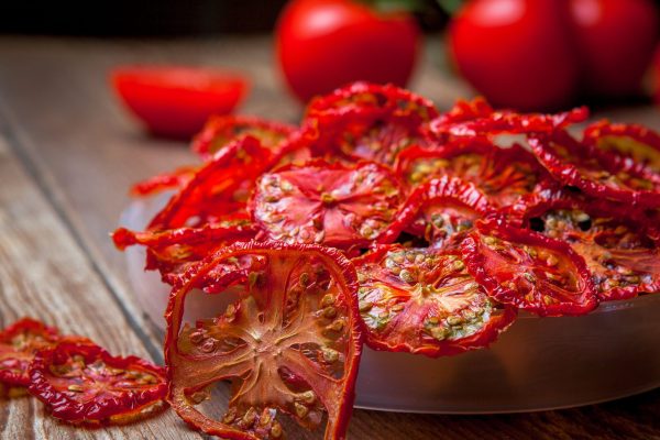 Side view close-up dried tomatoes in plate and fresh tomatoes on wooden table